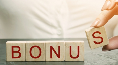 A hand placing the final letter 'S' to complete the word 'BONUS' spelled out on wooden blocks. 