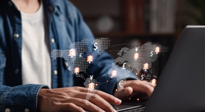 A person typing on a laptop with a digital overlay of a world map and global currency symbols