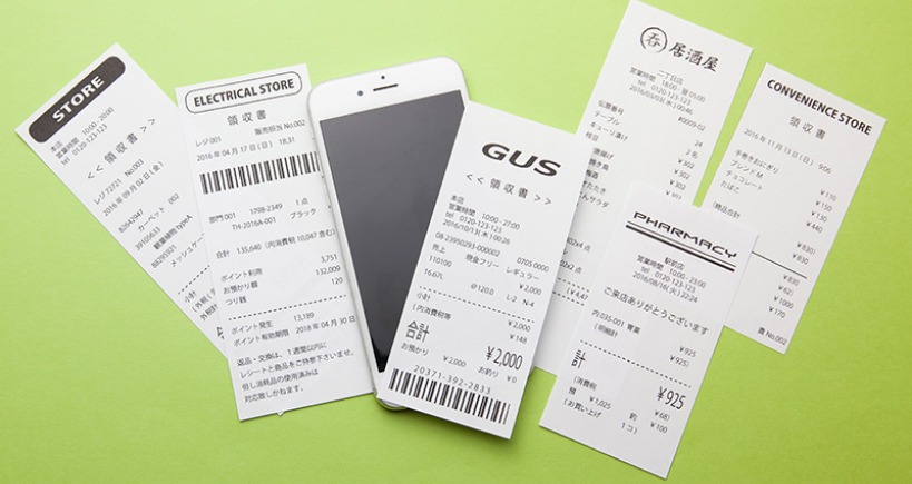 A green background with 5-6 shopping receipts and a smartphone casually placed on it.