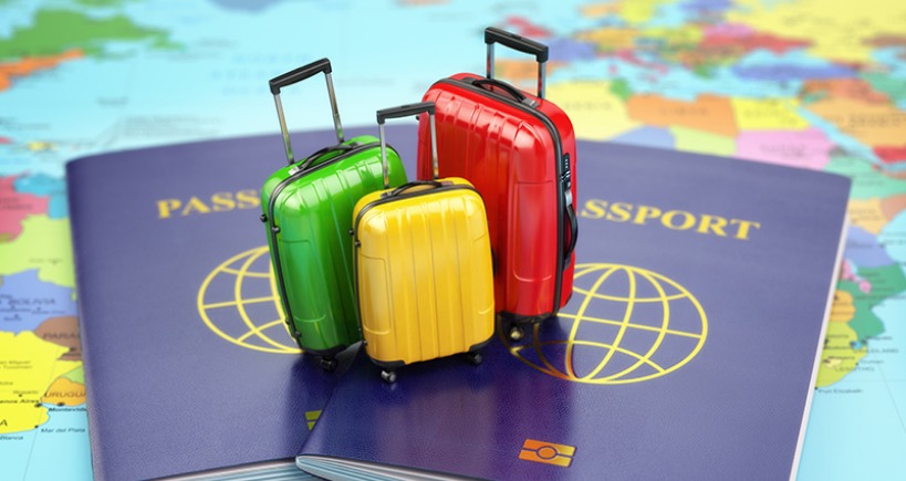 Two passports on a world map, with three miniature suitcases (green, yellow, red) placed on top of them.
